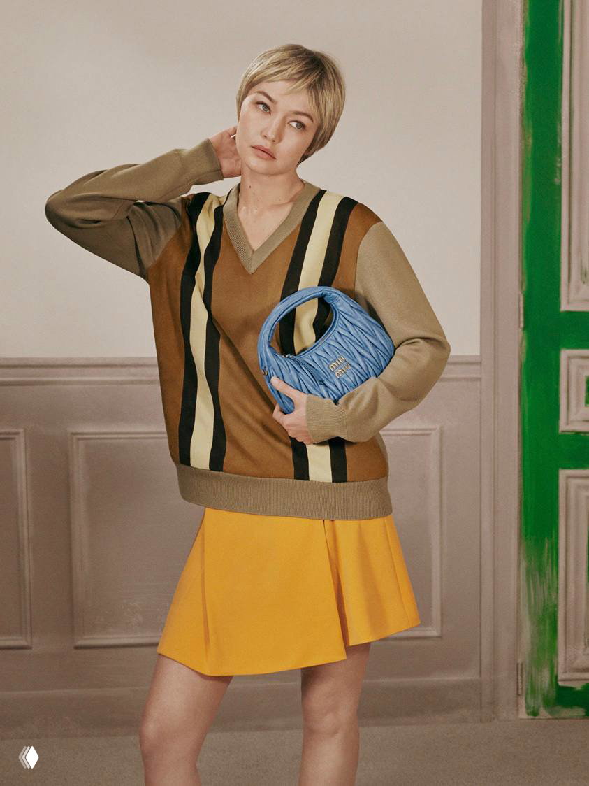 Модель в коротком парике в полосатом свитере и жёлтой юбке держит голубую сумку — живой кадр кампейна, демонстрация цветовых сочетаний.