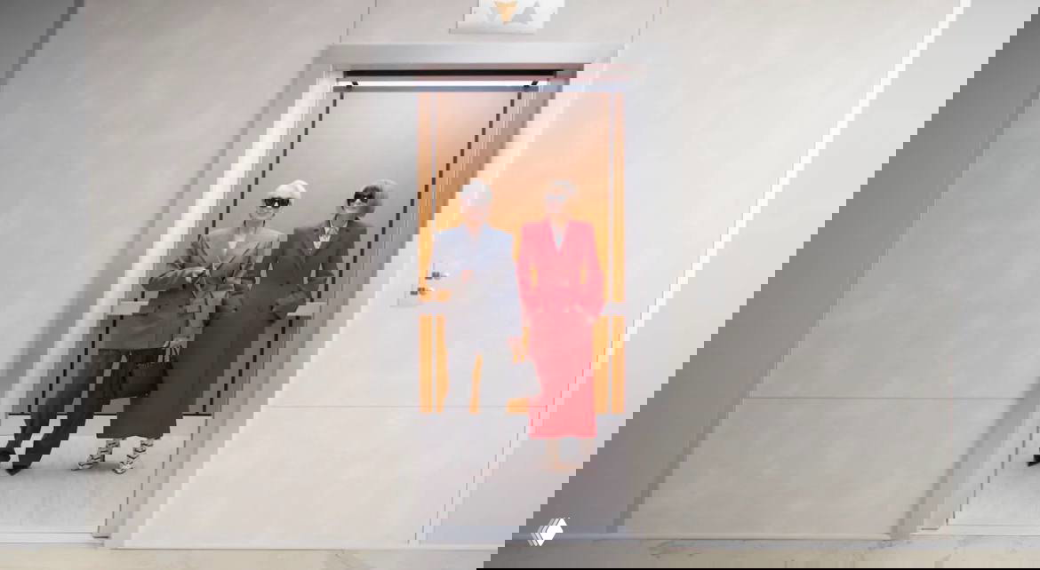 Анна Винтур и Мэрил Стрип выходят из лифта в строгих пальто и костюмах, стилизованные образы и официальный интерьер на заднем плане