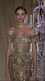 Модель в платье Zuhair Murad с роскошной золотой вышивкой и открытыми плечами, показ кутюрной коллекции на подиуме.