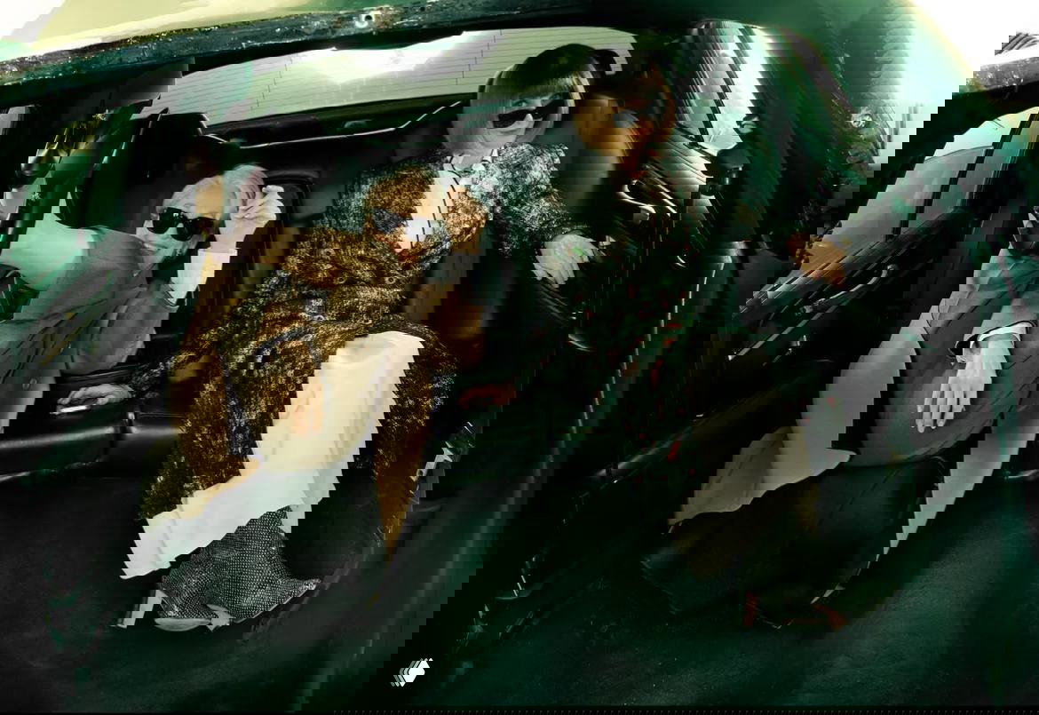 Кадр в салоне автомобиля: Анна Винтур и Мэрил Стрип в расслабленных позах, модные ботинки и пальто на фоне чёрного интерьера машины