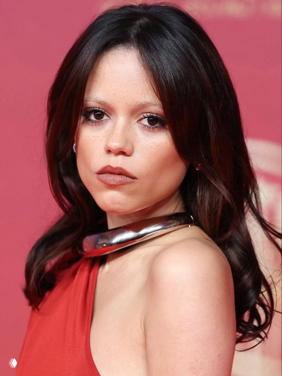 Крупный план лица и верхней части туловища: металлический широкий чокер, макияж в натуральных тонах и волнистые тёмные волосы.