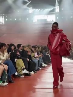 Модель в ярком алом комплекте идёт по подиуму Lacoste на Неделе моды в Париже: насыщенный монохромный образ и залы с приглушённым светом.