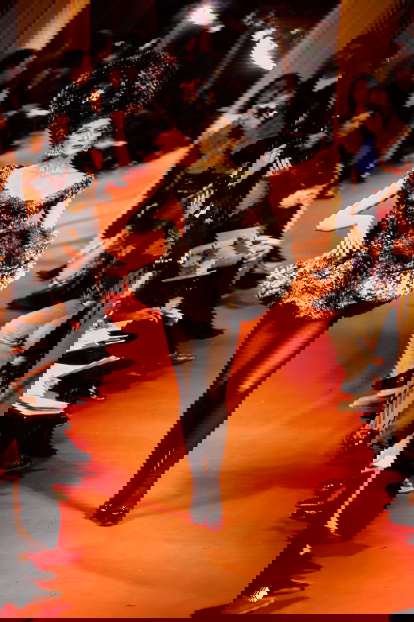 Модель в коротком черном меховом платье с открытыми плечами шагает по красной дорожке на показе Vivienne Westwood осень 1993.