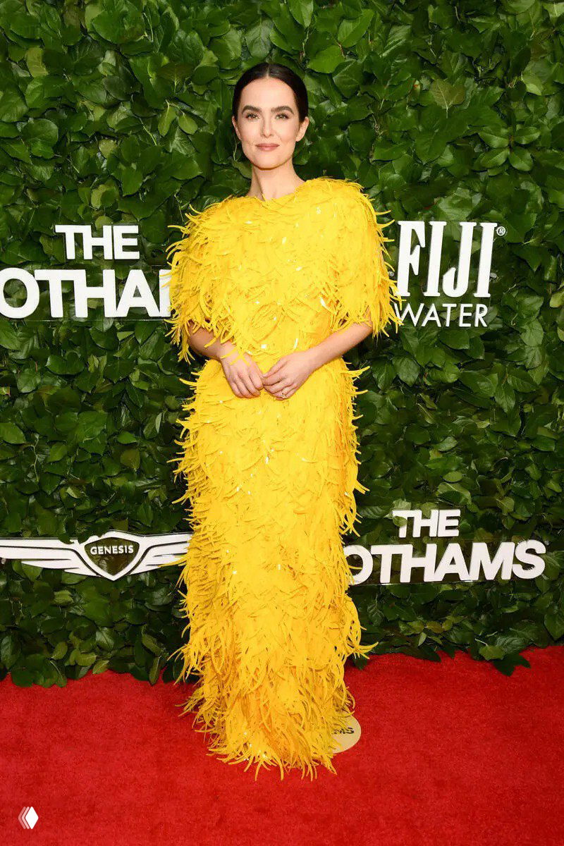 Зои Дойч в жёлтом платье с перьями на фоне зелёной декорации Gotham TV Awards 2025: яркий модный образ на красной дорожке.