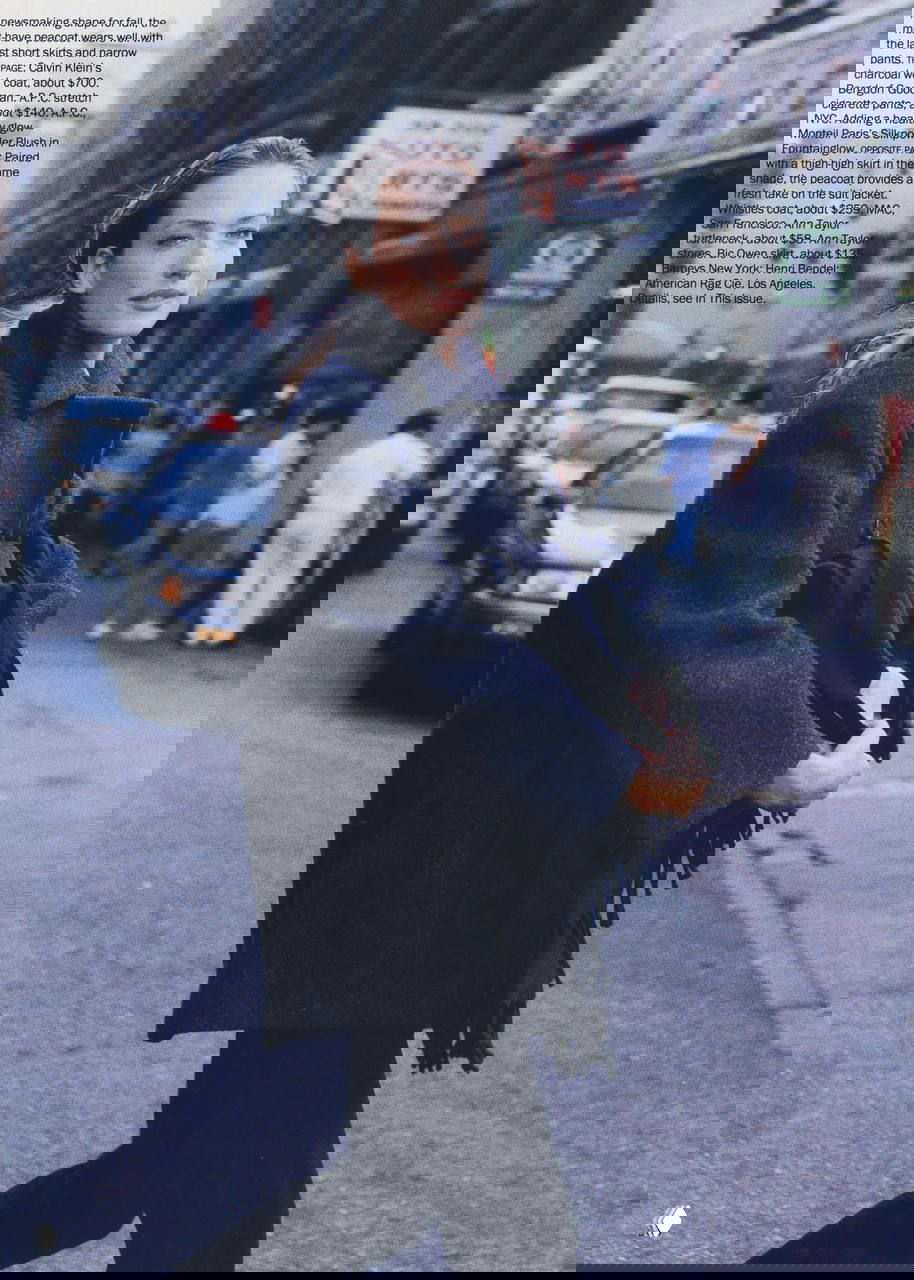 Модель в тёмном пальто идёт по улице с городским трафиком позади, строгий силуэт и атмосферный городской фон 90-х.