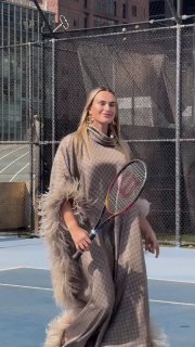 Арина Соболенко на теннисном корте в образе Primadonna из дебютной коллекции Демны: перья, накидка и ракетка на фоне забора.