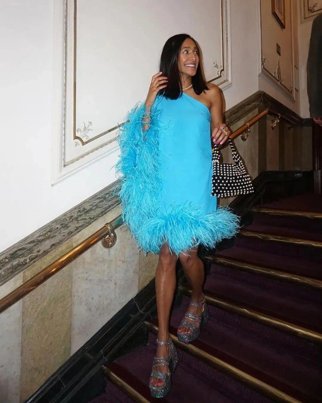 Девушка в коротком голубом платье с перьями спускается по лестнице; игривый и лёгкий праздничный образ с блеском в обуви.