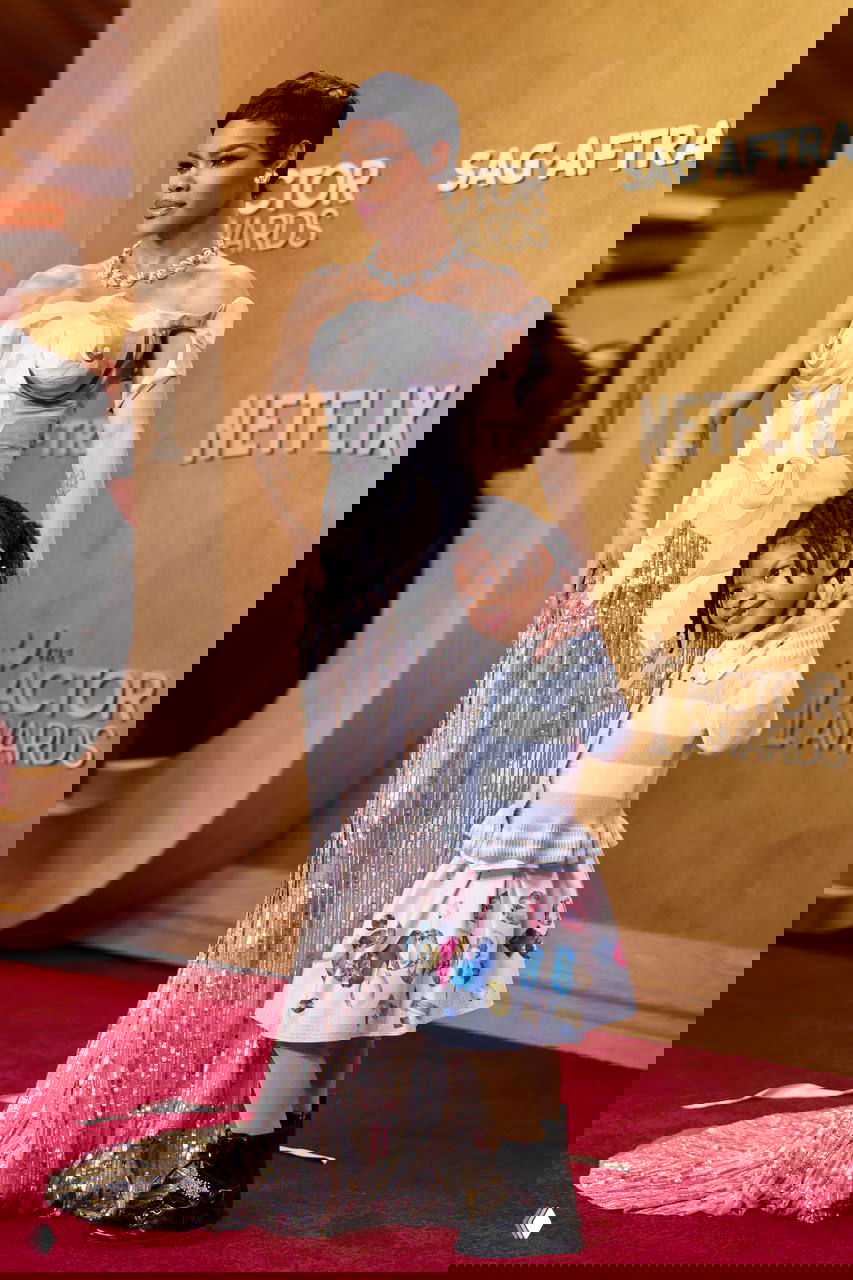 Фигура в блестящем платье с фактурным корсетом и ребёнок рядом: позирование у золотой фотозоны и логотипа премии SAG.