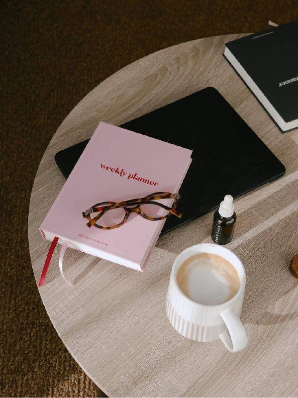 Женщина в джинсах сидит у окна рядом с ноутбуком и настольной лампой, задумчиво смотрит в сторону — момент паузы во время работы.