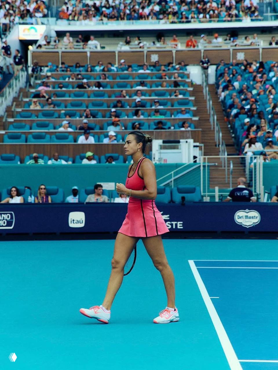 Арина Соболенко идёт по корту в розовом платье после одного из розыгрышей на турнире в Майами; внизу видно корт и заполненные места трибун.