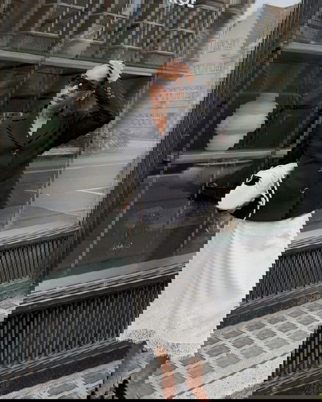 Городской образ: чёрный жакет и белая юбка с кружевной окантовкой на подоле — минималистичный рококо‑акцент в уличной моде.