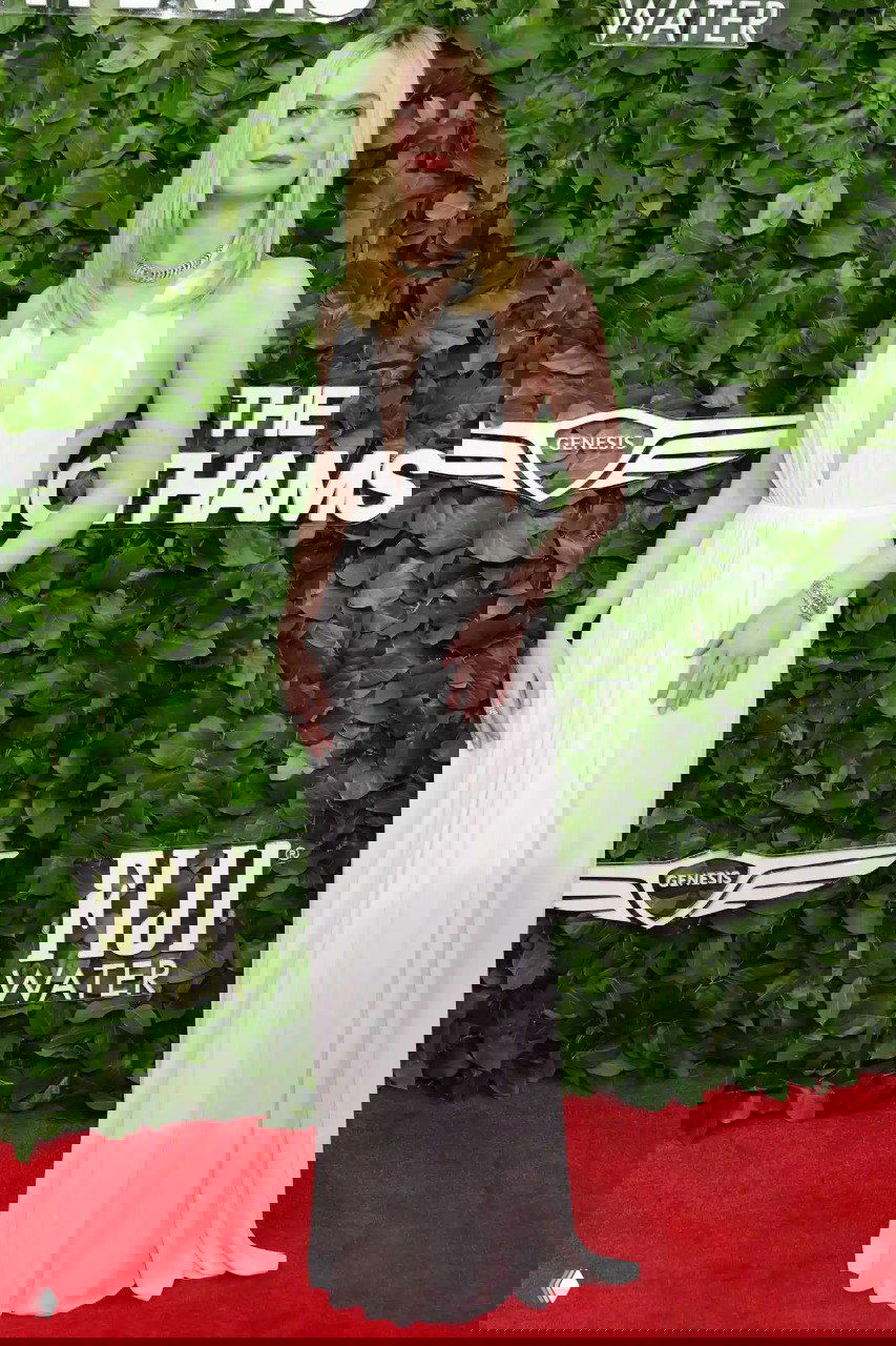 Эль Фаннинг в лёгком белом платье с глубоким вырезом на красной дорожке Gotham TV Awards 2025: романтичный минималистичный образ на фоне декорации.