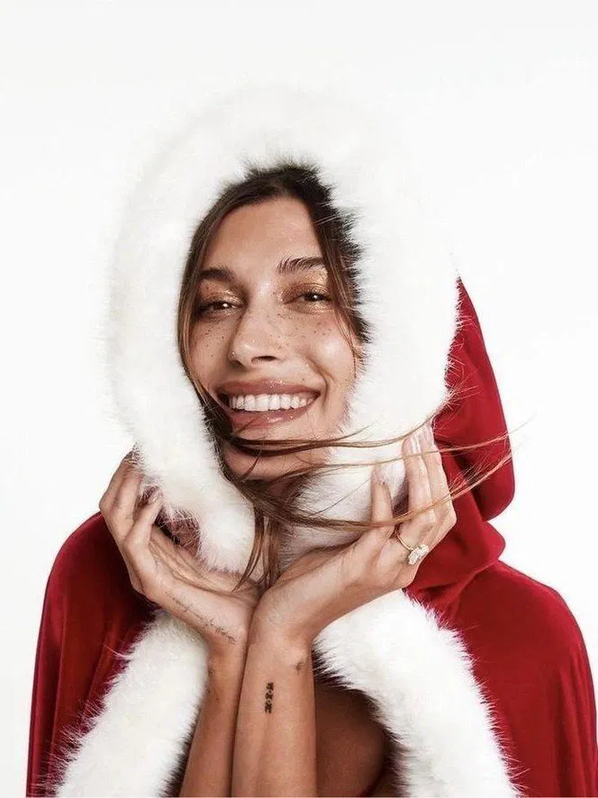 Улыбающаяся женщина в красном капюшоне с белой меховой отделкой — крупный план лица с лёгким натуральным макияжем и праздничным настроением.