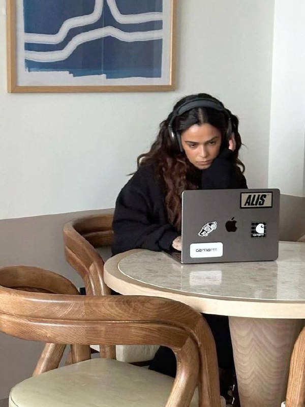 Вид сверху на круглый стол с ноутбуком, книгами, чашкой и наушниками — совместная рабочая сессия или коворкинг.