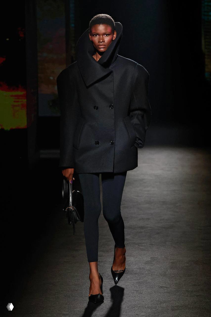 Модель на подиуме в тёмном объёмном структурном жакете с выраженными широкими плечами, смелый осенний образ из коллекции бренда.
