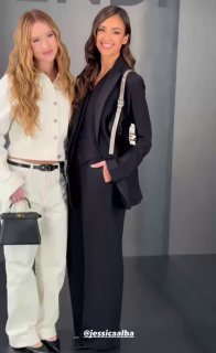 Две женщины в стильных образах позируют у нейтрального фона: снимок из фотозоны показа, демонстрирующий уличный и вечерний стиль гостей модного шоу.