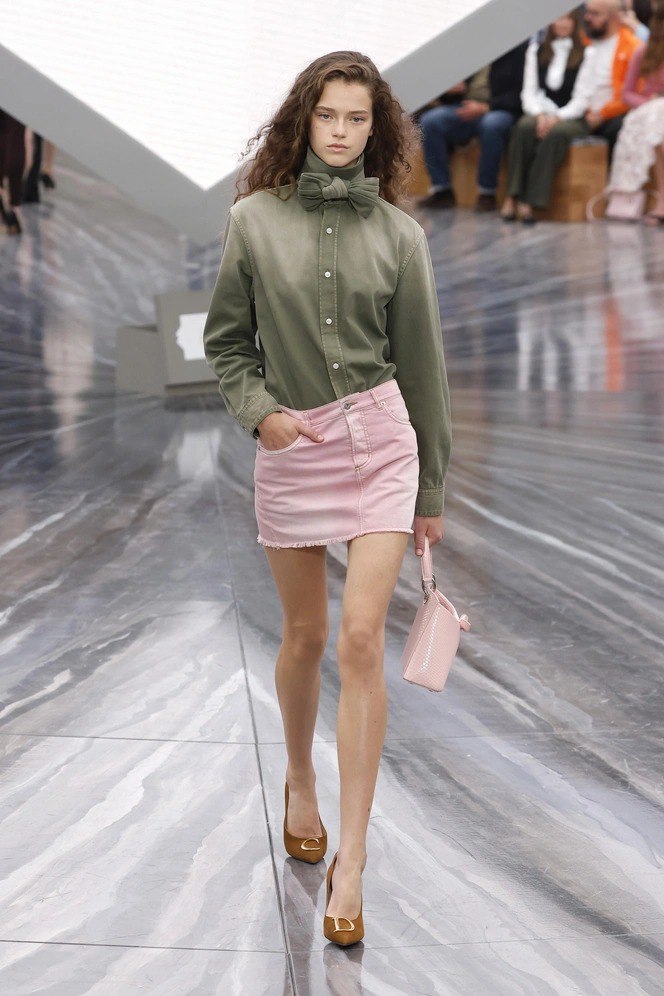 Модель в розовой джинсовой мини‑юбке и оливковой рубашке, сочетание йогуртово‑розового и пастельных оттенков в весенней коллекции.