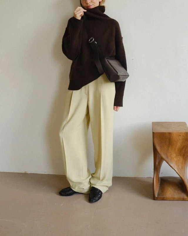 Модель в объёмном шоколадном свитере и бледно‑жёлтых широких брюках, чёрные туфли и сумка на поясе на нейтральном фоне — сочетание chocolate brown и pale yellow.