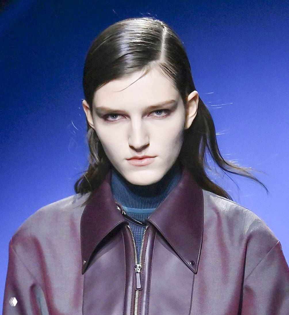 Модель с зачесанными назад волосами в темной кожаной куртке и строгим воротником — образ с показа в Париже