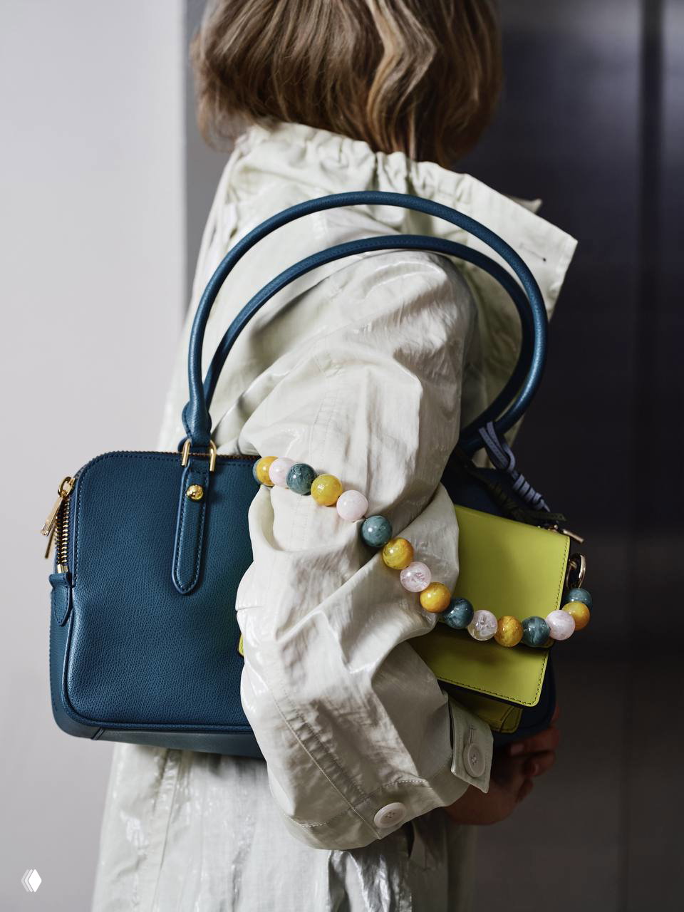 Крупный план двух сумок на плече модели: тёмно‑синяя кожаная сумка и салатовая мини‑сумка с ремнём из крупных разноцветных бусин, акцент на деталях.