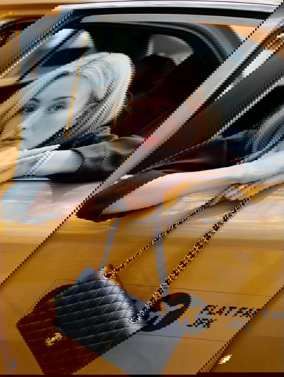 Сара Пиджон опирается на окно жёлтого такси, в руках сумка Chanel; портретный кадр из нью‑йоркской съёмки с фокусом на аксессуарах и эмоции модели.