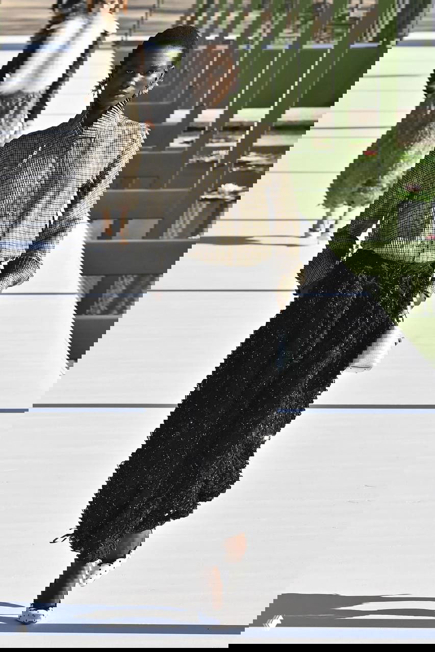 Темнокожая модель идёт по дорожке в комбинированном образе: рубашка в клетку и фактурная юбка — сочетание строгости и текстильной игры в коллекции Джонатана Андерсона.