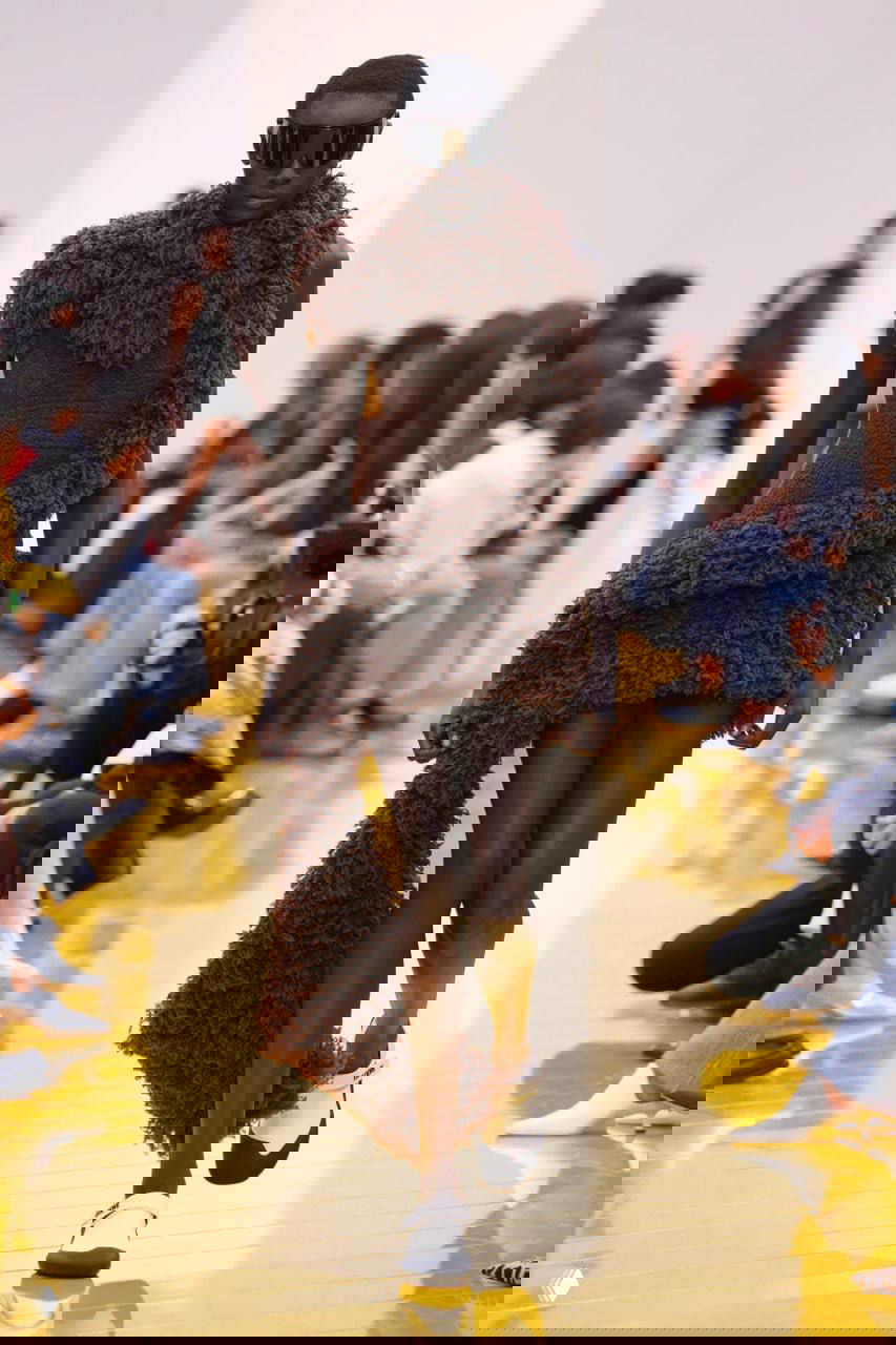 Тёмная модель в коричневом пушистом мини‑платье со шлейфом, текстура напоминает мягкий ворс — игра с объёмом и уютной эстетикой коллекции.