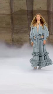 Модель на подиуме показа Chloé в многослойном светло-голубом платье с воланами; минималистичный фон и туманная атмосфера на шоу.