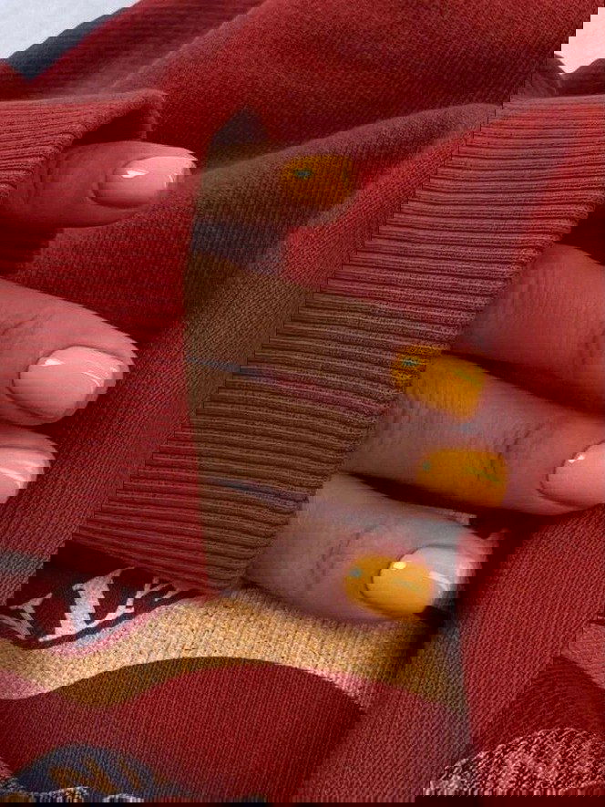 Короткие ногти ярко-жёлто-оранжевого оттенка, пальцы на фоне тёплого красного свитера — контрастный и уютный праздничный вариант.