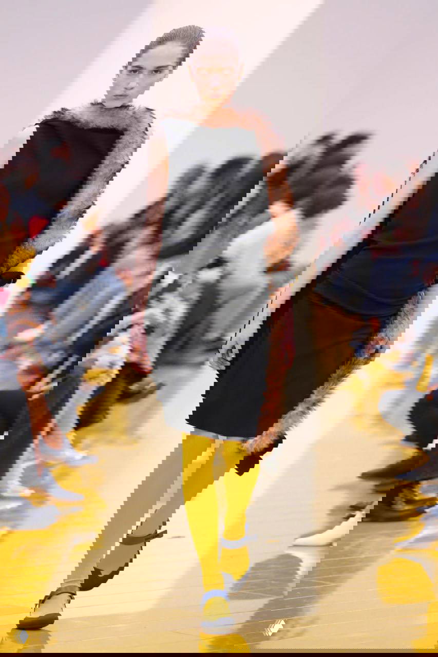 Элегантный образ: чёрное платье с меховой отделкой и ярко‑жёлтые колготы, сочетание текстур и цвета на подиуме Loewe в рамках коллекции.