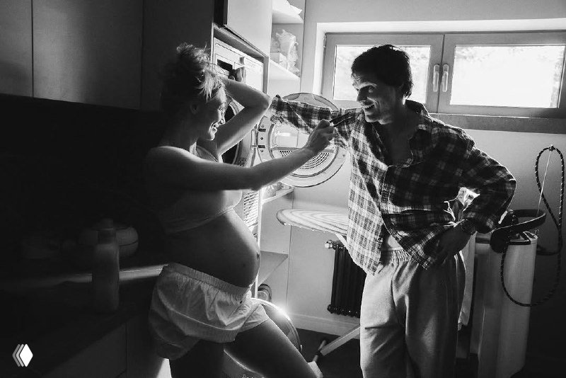 Чёрно‑белая фотография: Оксана в домашней обстановке с отчётливо видимым животом, Данила шутливо взаимодействует с ней — интимный бытовой кадр.