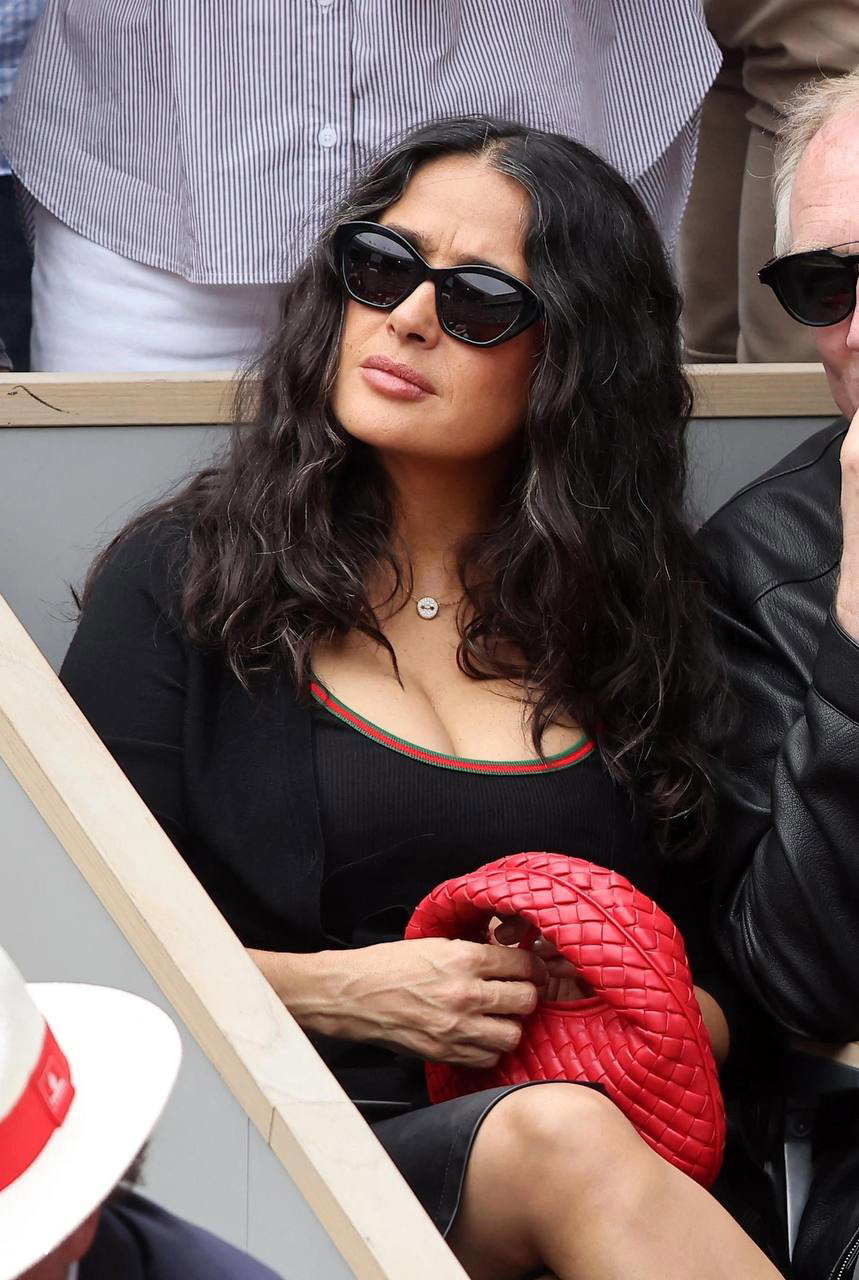 Крупный план женщины в чёрном: чёрный топ с красной окантовкой и компактная красная сумка Bottega Veneta на коленях.