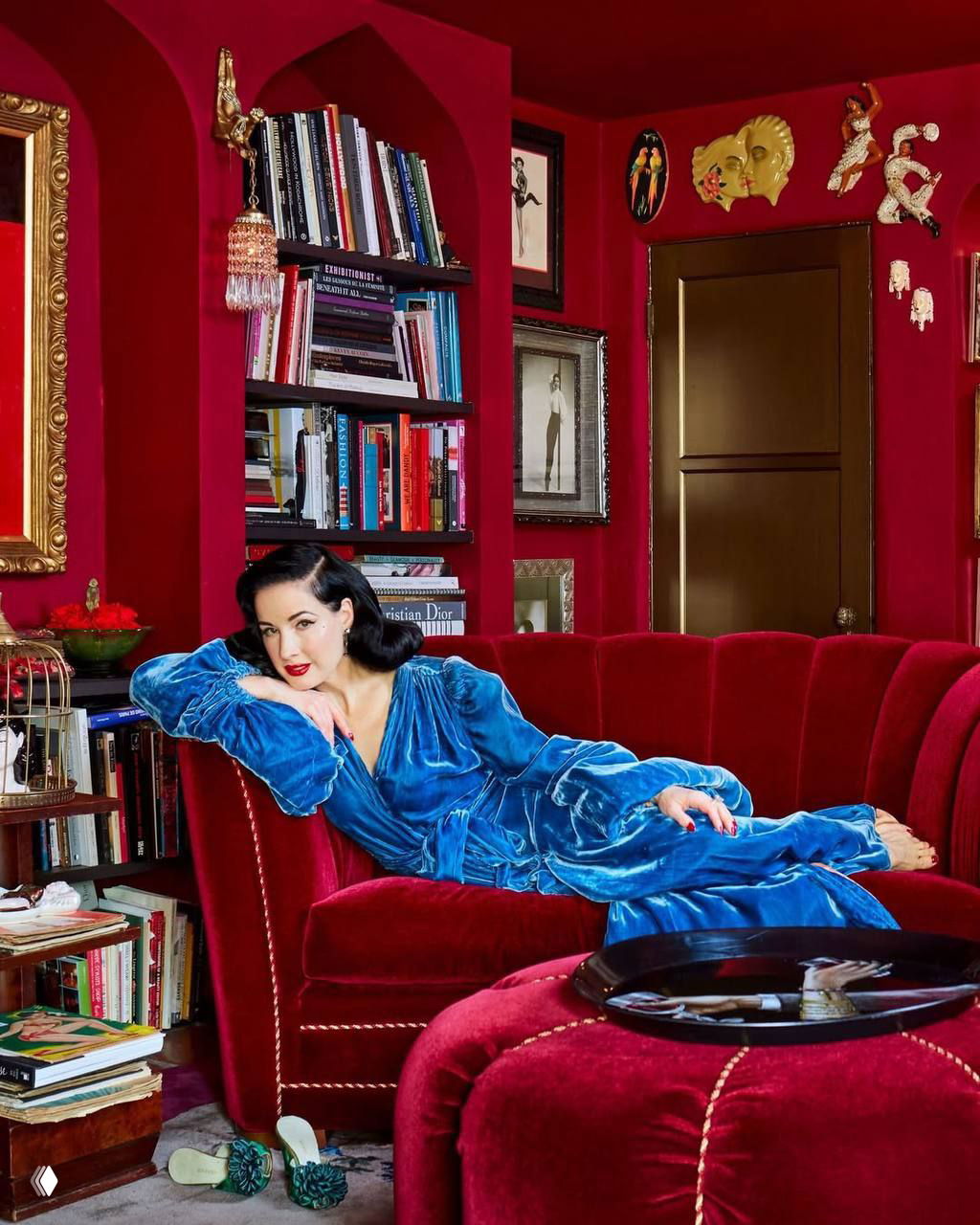 Гостиная или библиотека с ярко-красными стенами, бархатной мебелью и стеллажами с книгами — богатая декоративная сцена в тёплых тонах.