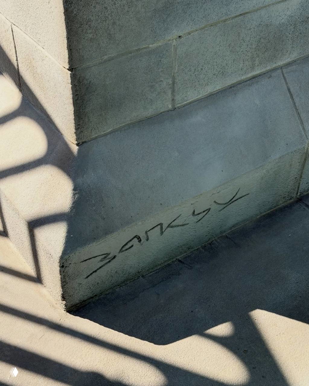 Надпись «Banksy» граффити на каменном цоколе рядом со ступенями; тени от перил и фактура камня, район Сент-Джеймс, Лондон.