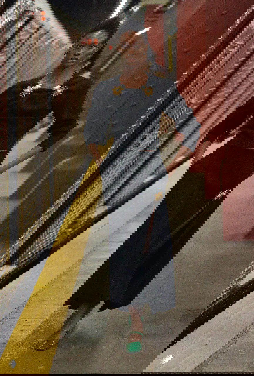 Модель в чёрном элегантном платье с крупными брошами идет по платформе нью‑йоркского метро во время показа Chanel от Матье Блази.