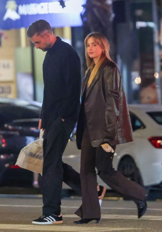 Ночной тематический кадр: двое в тёплых верхних вещах и кожаной куртке, прогулка по освещённой улице города.