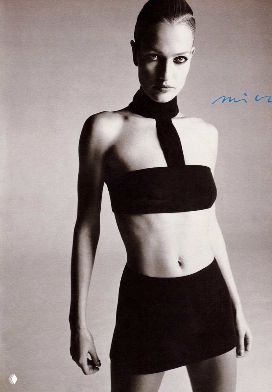 Студийный портрет в монохроме: модель в коротком топе и мини‑юбке, высокая талия и акцент на осанке, утончённая мода 1990‑х.