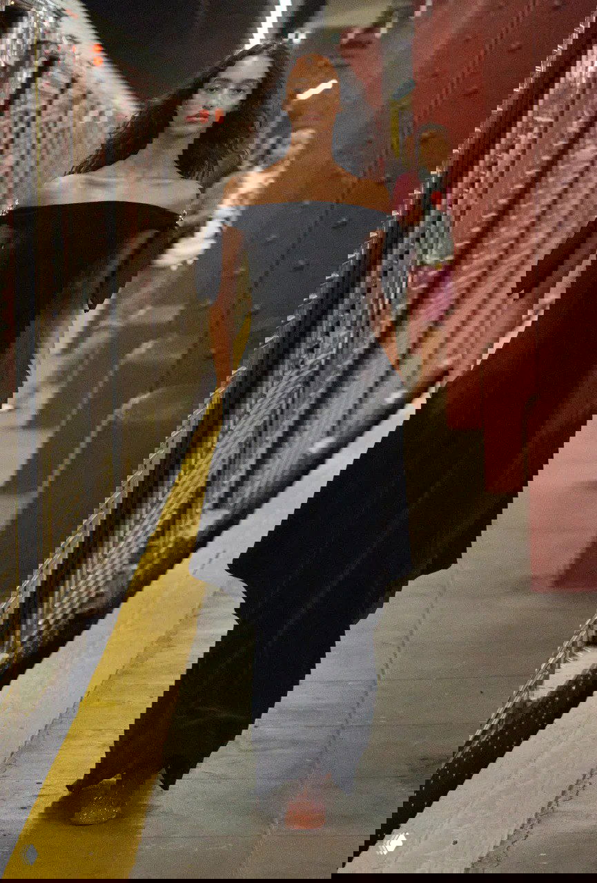 Модель в открытом чёрном платье без бретелей идет по платформе нью‑йоркской станции, фон — рельсы и вагон метро на показе Chanel.