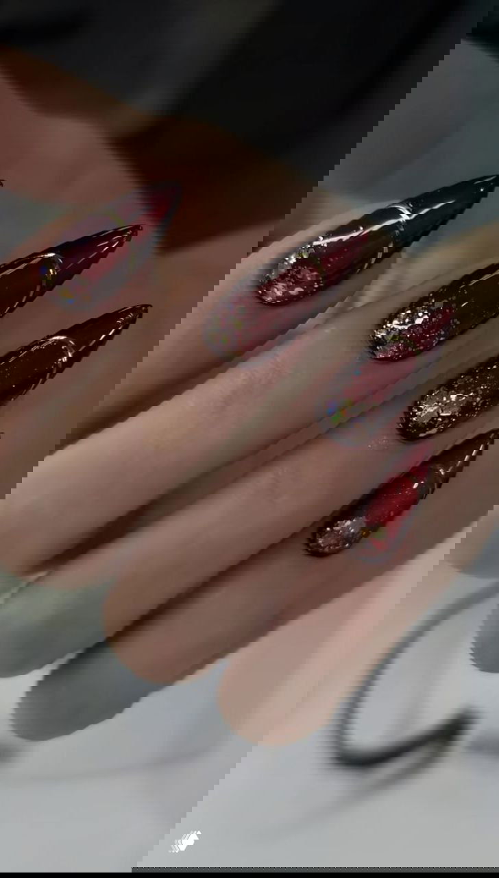 Близкий план тёмно‑красных ногтей с золотыми полосками и крупными сияющими кристаллами на безымянном пальце, студийная подсветка.