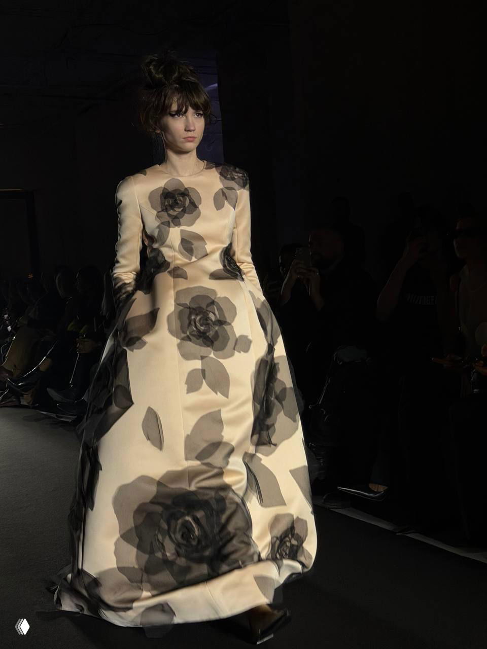 Модель в кремовом бальном платье с крупными полупрозрачными черными розами — флористический принт на фоне темного пространства.