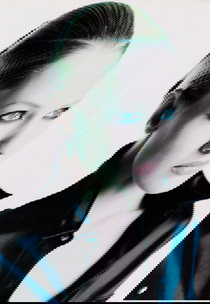 Портрет в пол‑оборота: лицо и плечи модели на светлом фоне, холодный контраст и высокий охват света для подчёркивания черт лица.