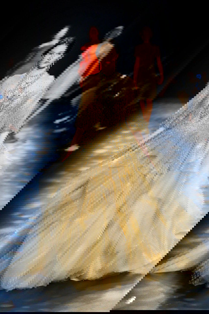 Большое золотистое бальное платье Marchesa с многослойной юбкой и мерцающей вышивкой, образ в пастельных золотых тонах на показе.