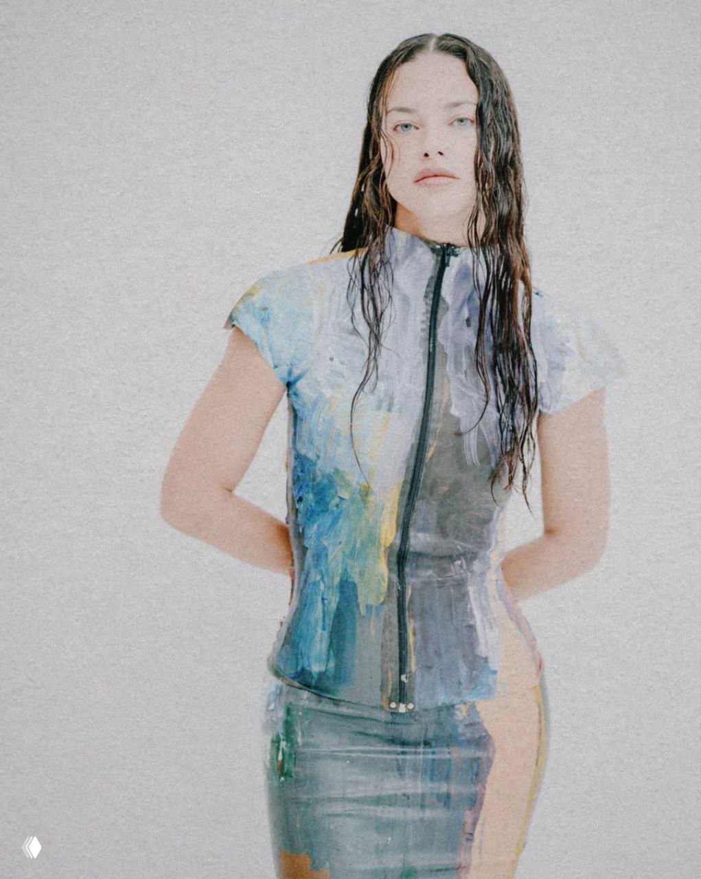 Модель в коротком топе и юбке с эффектом красочной живописи; художественная стилизация, яркие мазки и контраст с нейтральным фоном.