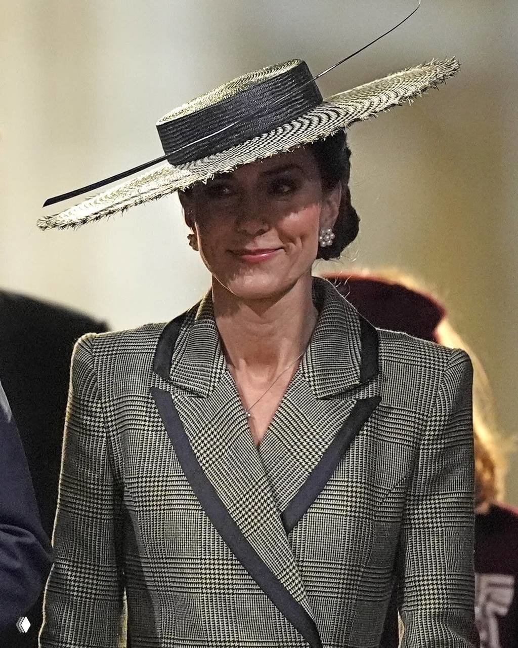 Женщина в твидовом жакете и широкой соломенной шляпе снята анфас в помещении; подчеркнуты силуэт шляпы и детали образа.