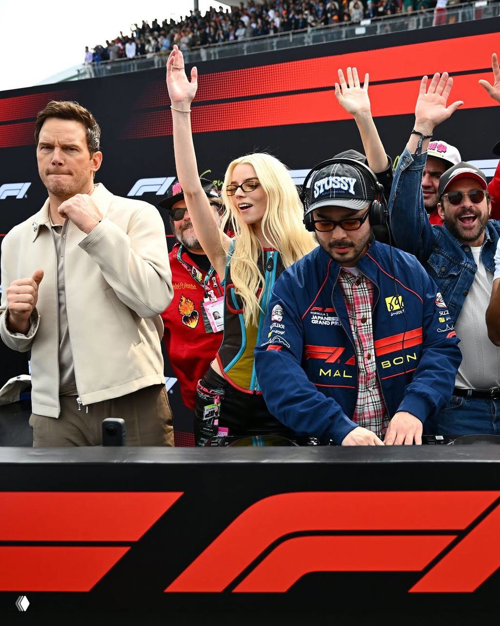 Группа актёров и приглашённых гостей на стартовой линии Гран‑при в Сузуке, поднимают руки и празднуют прямо на асфальте во время уик‑энда