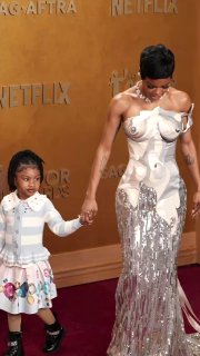 Тейяна Тейлор держит за руку пятилетнюю дочь Рю Роуз на ковровой дорожке; девочка помогает расправлять платье матери во время выхода на мероприятие.