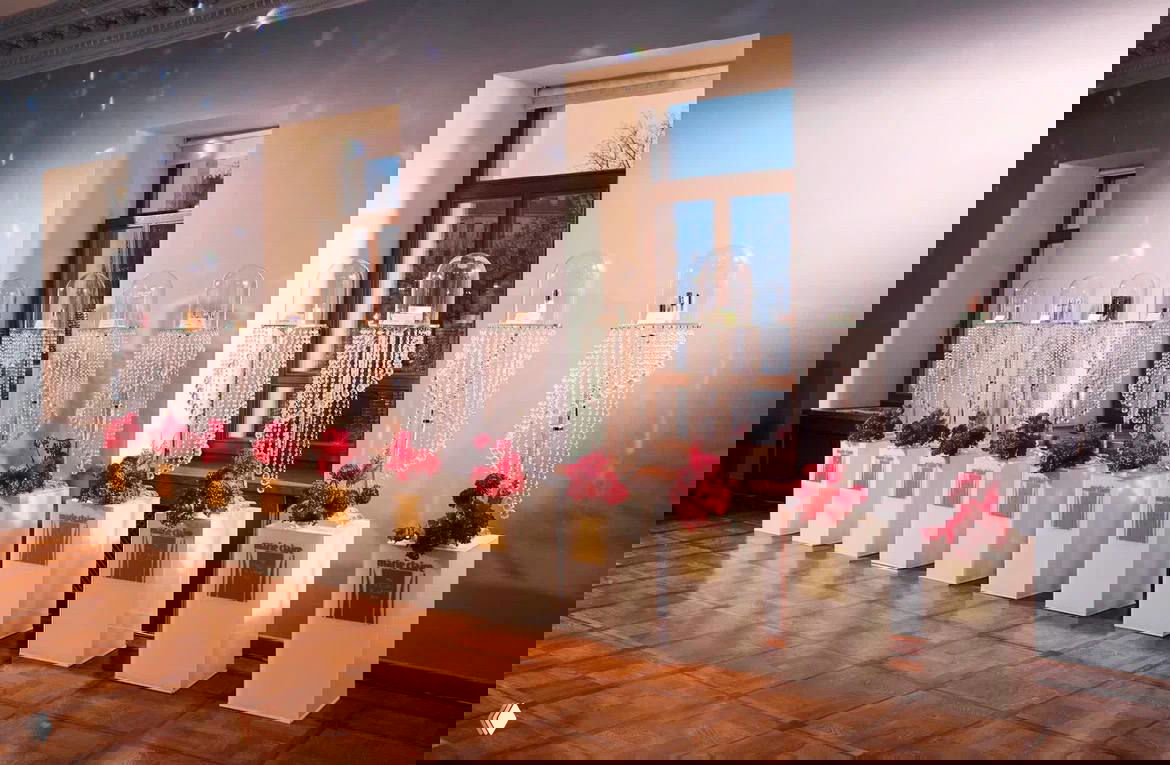 Ряд стеклянных колб с украшениями и декором на подиуме, оформление выставочной зоны с цветочными акцентами и кристальными элементами.