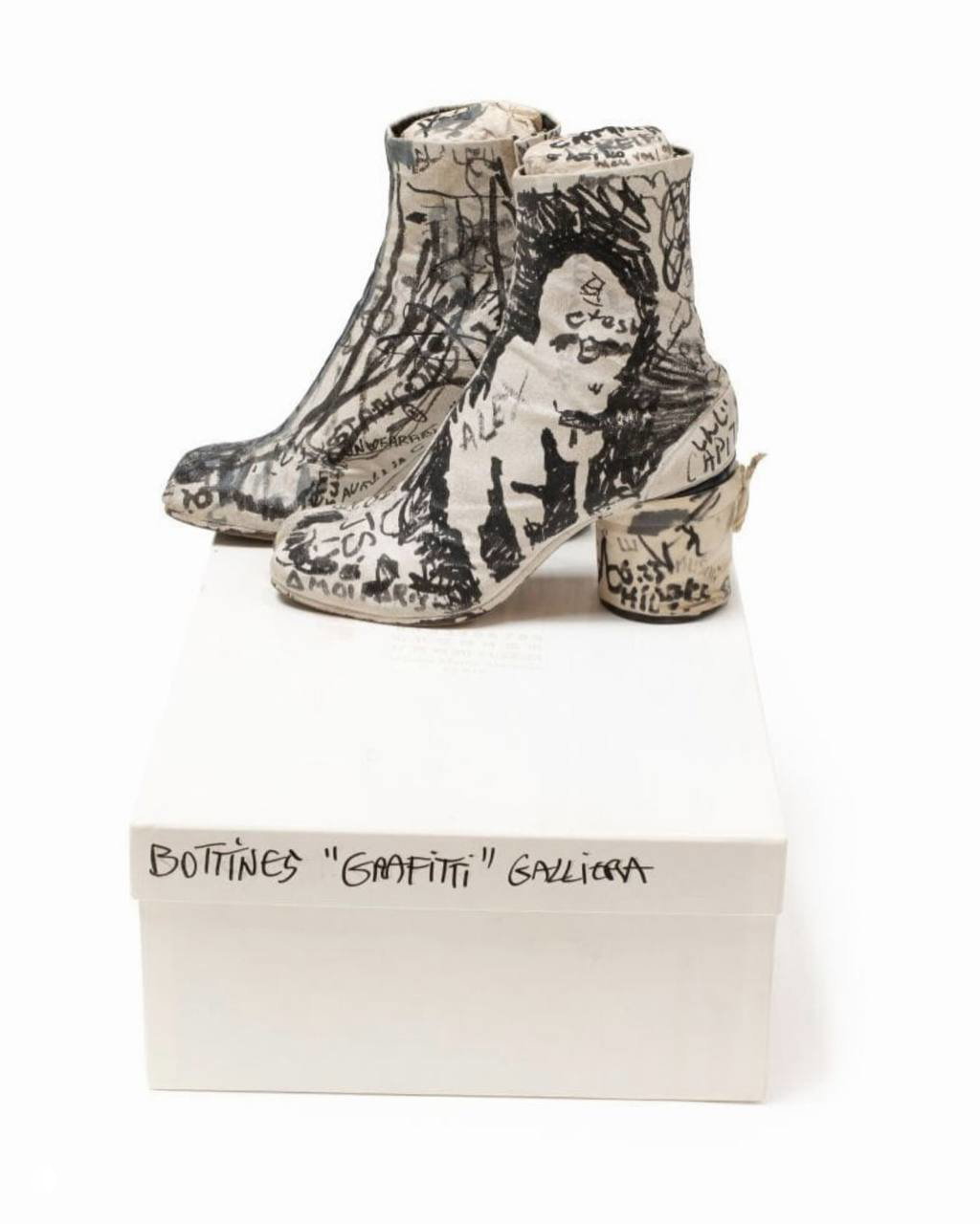 Таби Margiela на белой коробке с подписью «Bottines ‘Graffiti’ Galliera», обувь покрыта маркерами и изображением лица, показана в профиль