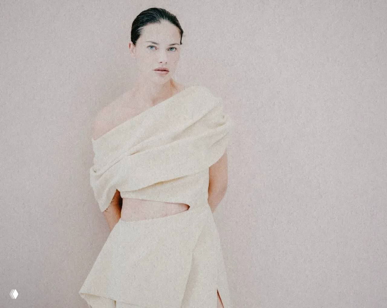 Портрет модели в светлом асимметричном костюме на бежевом фоне; минимализм формы и мягкая фактура ткани в фокусе снимка.