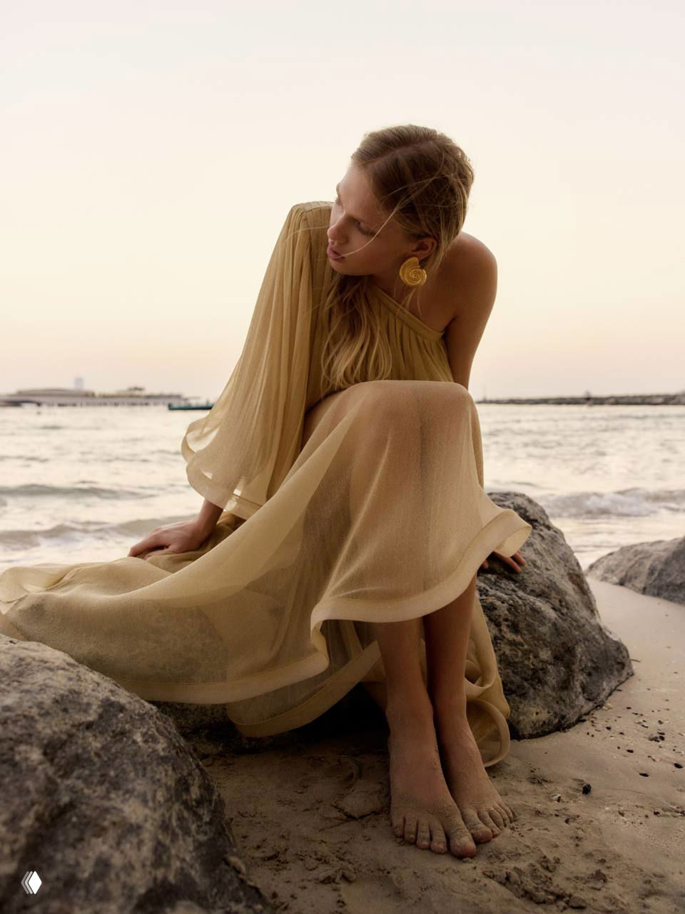 Дарья на морском берегу в бежевом прозрачном платье, сидящая на камнях; натуральные оттенки и мягкий закатный свет подчёркивают текстуру ткани.